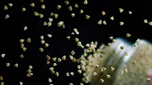 Closeup of Falling Down Green Buckwheat From Glass Jar on Black Background