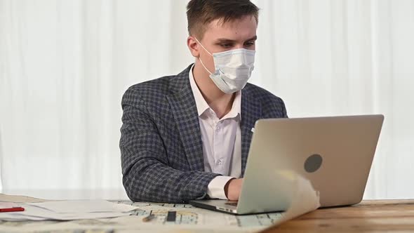 man has put protective mask on face and is working with drawings and plans