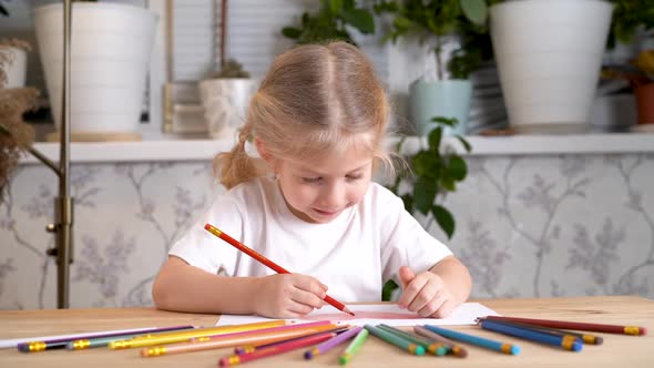 a Little Girl Enthusiastically Draws with Colored Pencils Sitting at the Table at Home Alone