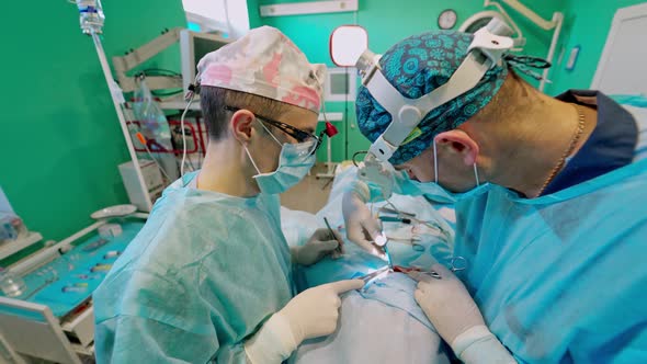 Surgeon and his assistant performing cosmetic surgery in hospital operating room