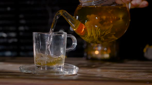 Flower Tea from a Glass Pot is poured into a Glass Cup in a Cozy Homely Atmosphere.