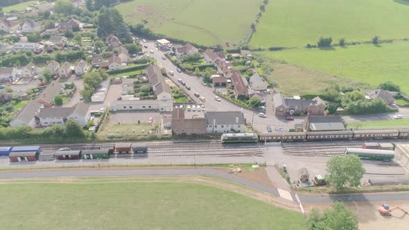 Sideways tracking aerial from right to left of a diesel train leaving or setting off from Washford t