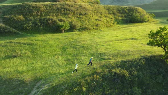 Two children running along the green hills in the sun. Aerial view, 4k, follow.