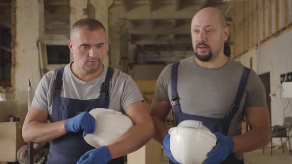 Two Adult Strong Caucasian Builders Walking at the Construction Site and Talking