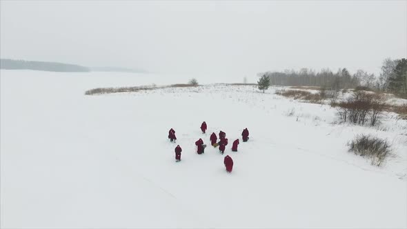 Group Of Monks In Hood Robe Walking Along Winter Snow Trail In Forest