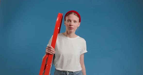 Beautiful Young Woman with a Hammer in Her Hands and a Stepladder