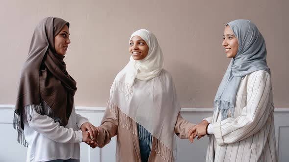 Three Muslim Girls Stand Holding Hands Talking and Smiling in Bright Studio