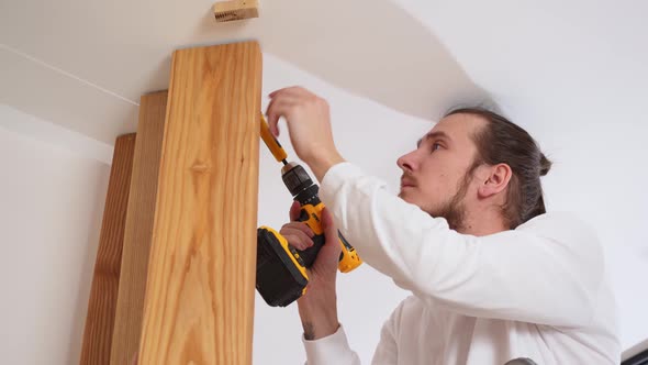 the Carpenter Screws with a Screwdriver Wooden Ash Lamellae to the Ceiling