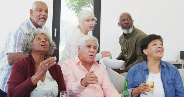 Happy senior diverse people watching tv with beer at retirement home