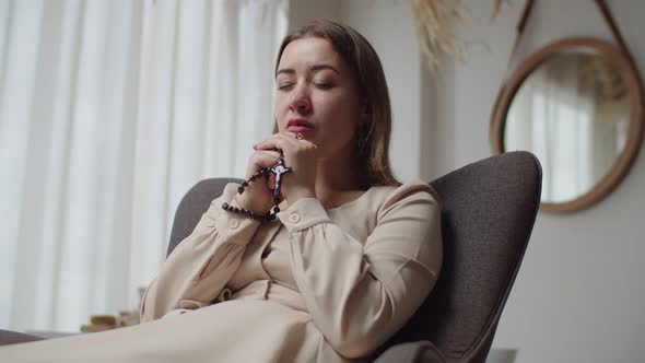 Attractive Woman with Eyes Closed Praying to God with Rosary Beads at Home