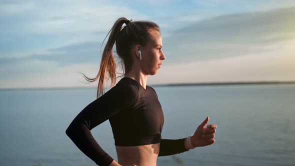 Athletic Sportswoman in Earphones Running on Beach at Sunset Slow Motion