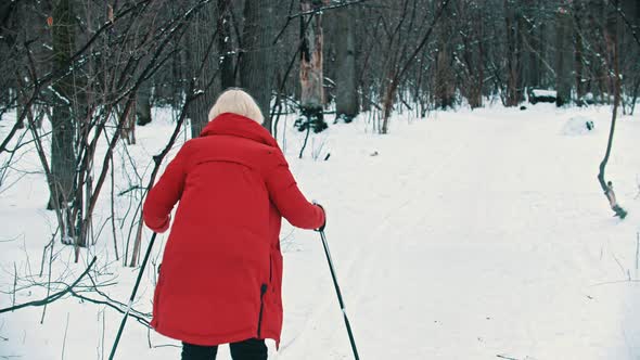 A Young Blonde Woman in Red Down Jacket Walking on Ski in the Woods