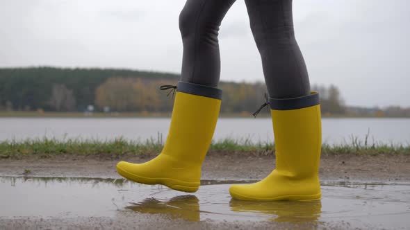 Legs Of A Woman In Yellow Boots Go Through Puddles On A Cloudy Autumn Day