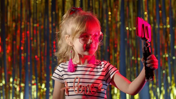 Child Kid Blogger Smiling Recording Video Blog Vlog on Smartphone in Night Club with Red Neon Light