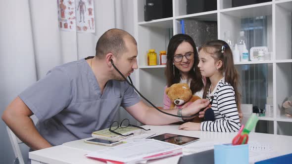 Male Doctor in the Office Takes Patients. The Family Doctor Examines a Little Girl Who's Mom Came alt