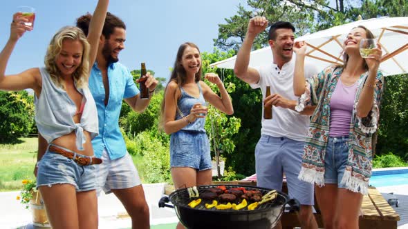 Group of friends dancing and having drinks while preparing barbeque