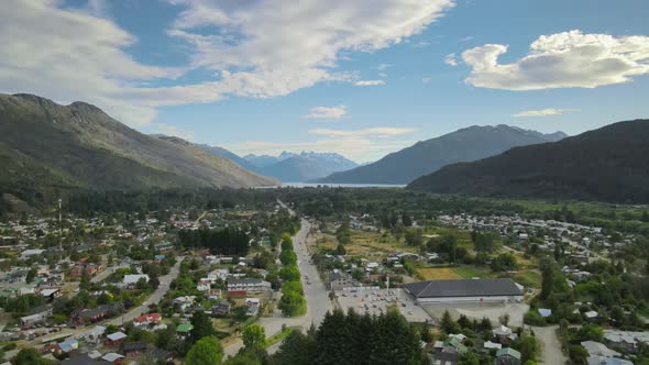 Dolly in flying above Lago Puelo village leading to a pine tree forest with lake and Andean mountain