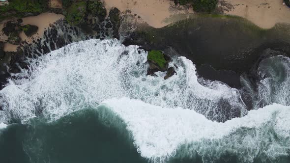 Top down aerial view of giant ocean waves crashing and foaming in coral beach