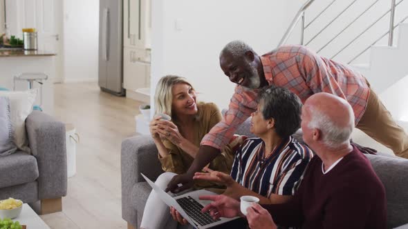 Two diverse senior couples sitting on a couch using a laptop and laughing