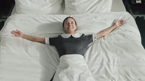 Housekeeper Lying on Bed in Hotel Room with Arms Spread