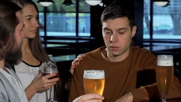 Friends Cheering Up Young Man, While Drinking Together at the Pub