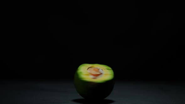 Female Hand Spinning Halved Avocado at Black Background on Table Leaving