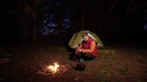 A Man Drinks Coffee Near a Bonfire