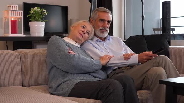 An Elderly Couple Sits in A Living Room in An Apartment and Watches Tv