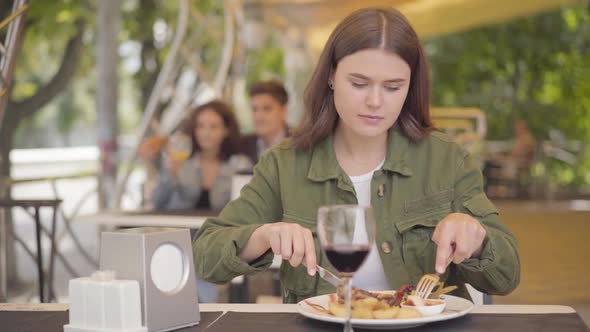 Young Beautiful Woman Eating Tasty Meat Dish with Potato Drinking Red Wine at Street Cafe