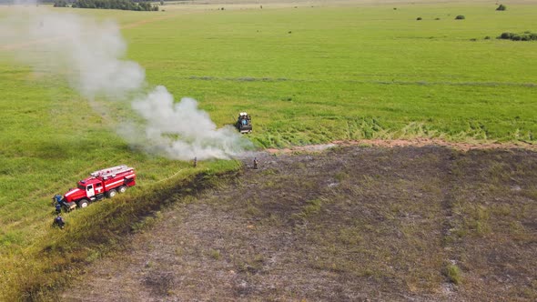 A Fire Truck and a Tractor on the Edge of a Burnt Field with Smoke