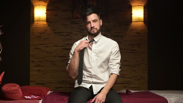 Young tired manager sits on a couch in a massage parlor and idly removes his tie