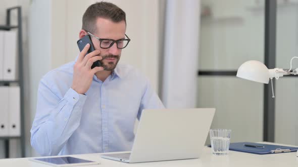 Middle Aged Man Talking on Smartphone While Working on Laptop