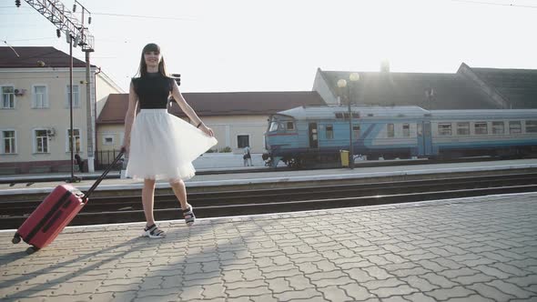 Happy Lady Goes Far with Suitcase and Poses with Dress on Railway Platform