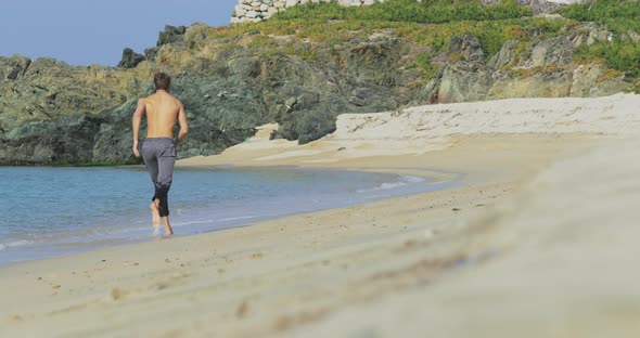 The Handsome Man with a Perfect Athletic Body in Gray Trousers Having Fun on a Deserted Beach in the