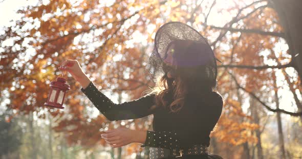 Attractive Woman in a Special Dress and Hat Looks Like a Witch in the Autumn Forest