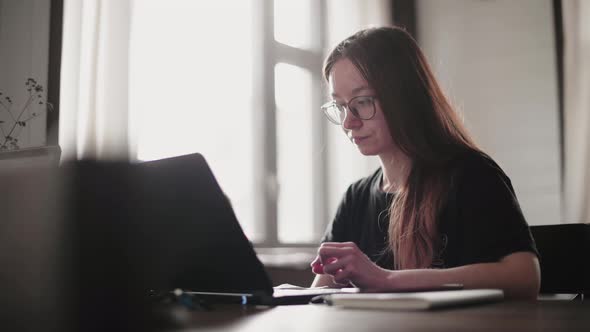 A young man and a young girl are working in front of laptops in their bright apartment.