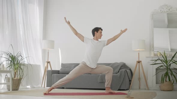 Man Practice Warrior Yoga Pose in Living Room. Sporty Man Doing Yoga for Body Care, Healthy Spine