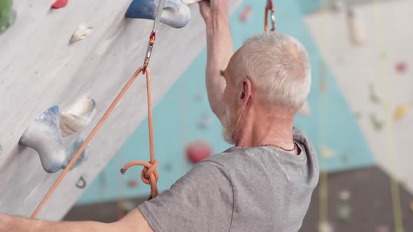 Old Athletic Climber Climbing on Cliff Indoors