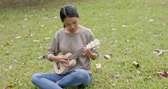 Asian Woman enjoy play ukulele and song in the park