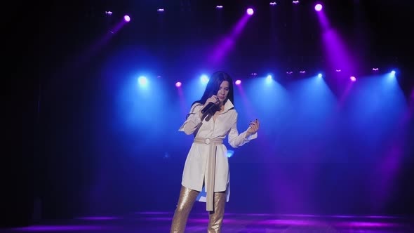 A Singer in a White Suit Singing on Stage with a Microphone in Her Hands