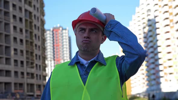 Engineer with Blueprint in Protective Helmet at Construction Site