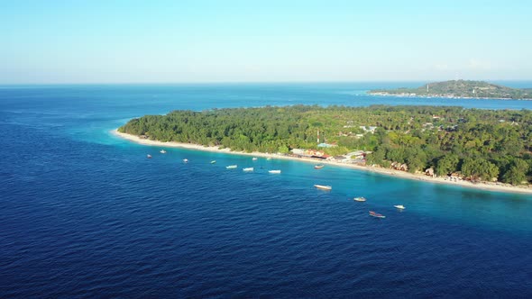 Tropical island cape contoured with white line of exotic beach surrounded by blue sea with boats anc