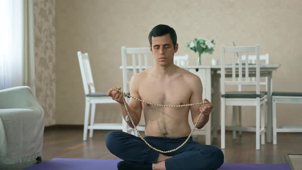 Man Meditates on Beads Sitting on the Floor