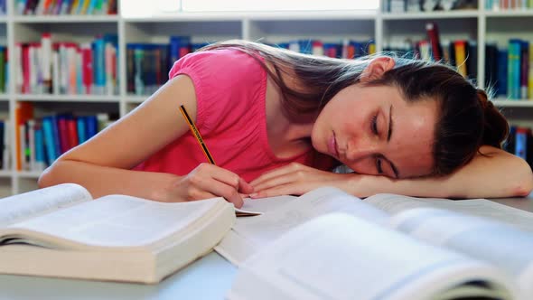 Tired schoolgirl sleeping in library while doing homework