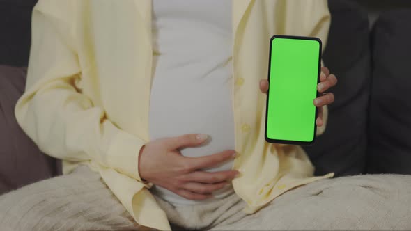 Pregnant Woman Holding Phone with Empty Green Screen at Home