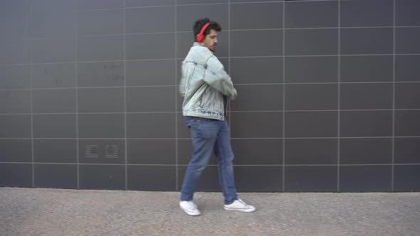 Man dancing while walking down the street, listening to music through a phone and red headphones