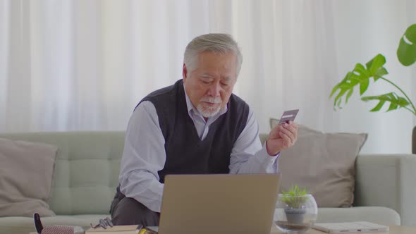 elderly asian man using computer laptop and using credit card to shopping online and payment at home