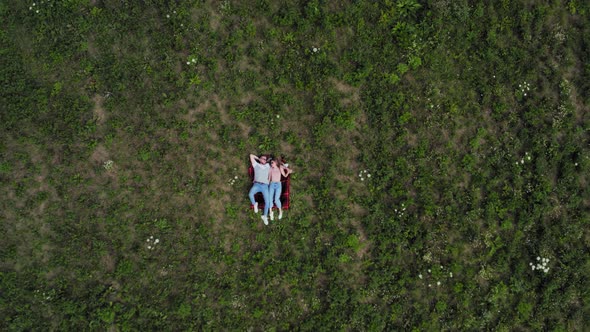 Happy Young Couple Lying on the Grass in the Meadow. The Camera Slowly Flies Away From Them. Aerial