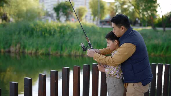 Asian Dad Shows His Son How to Cast a Fishing Rod on Practice Gives Instructions About Fishing