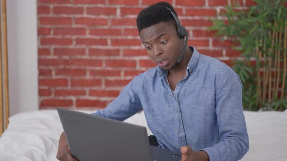 Confident African American Expert in Earphones Sitting on Bed Talking at Laptop Web Chat